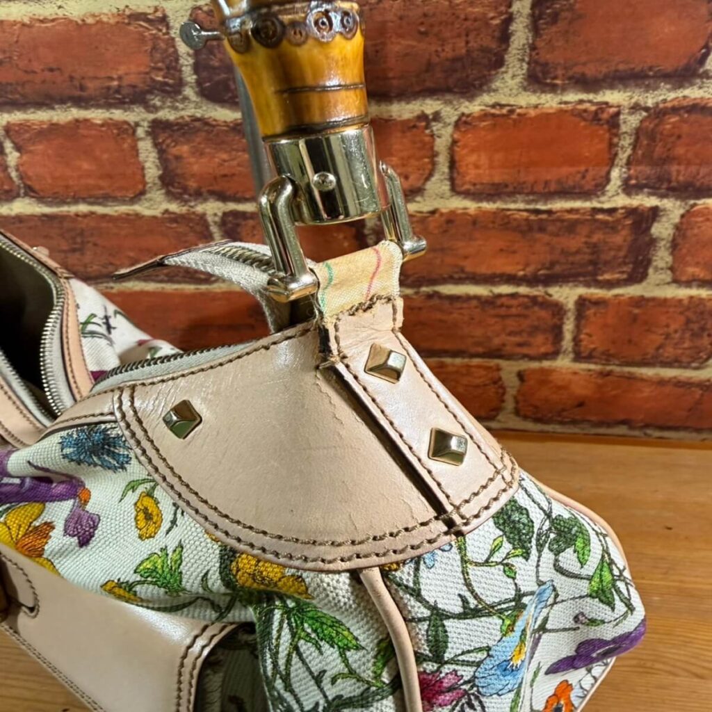 Floral-printed bag with beige leather trim, metal studs, and stitched seams.
