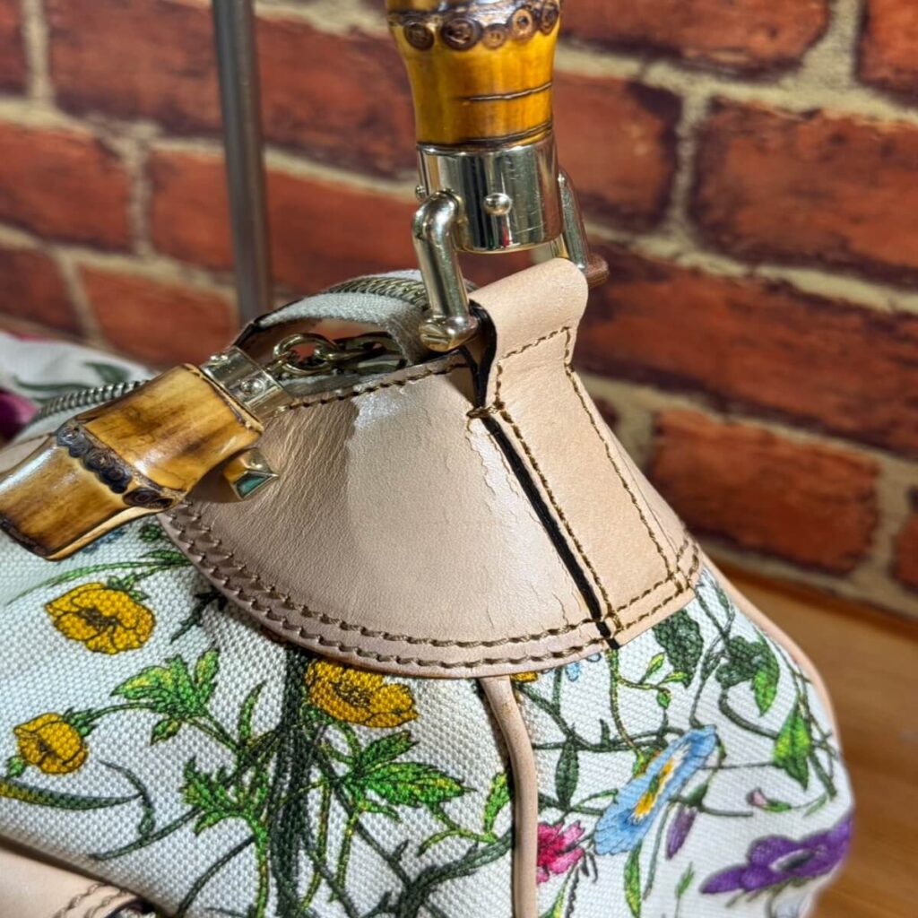 Close-up of a floral fabric bag with beige leather trim and metal hardware.