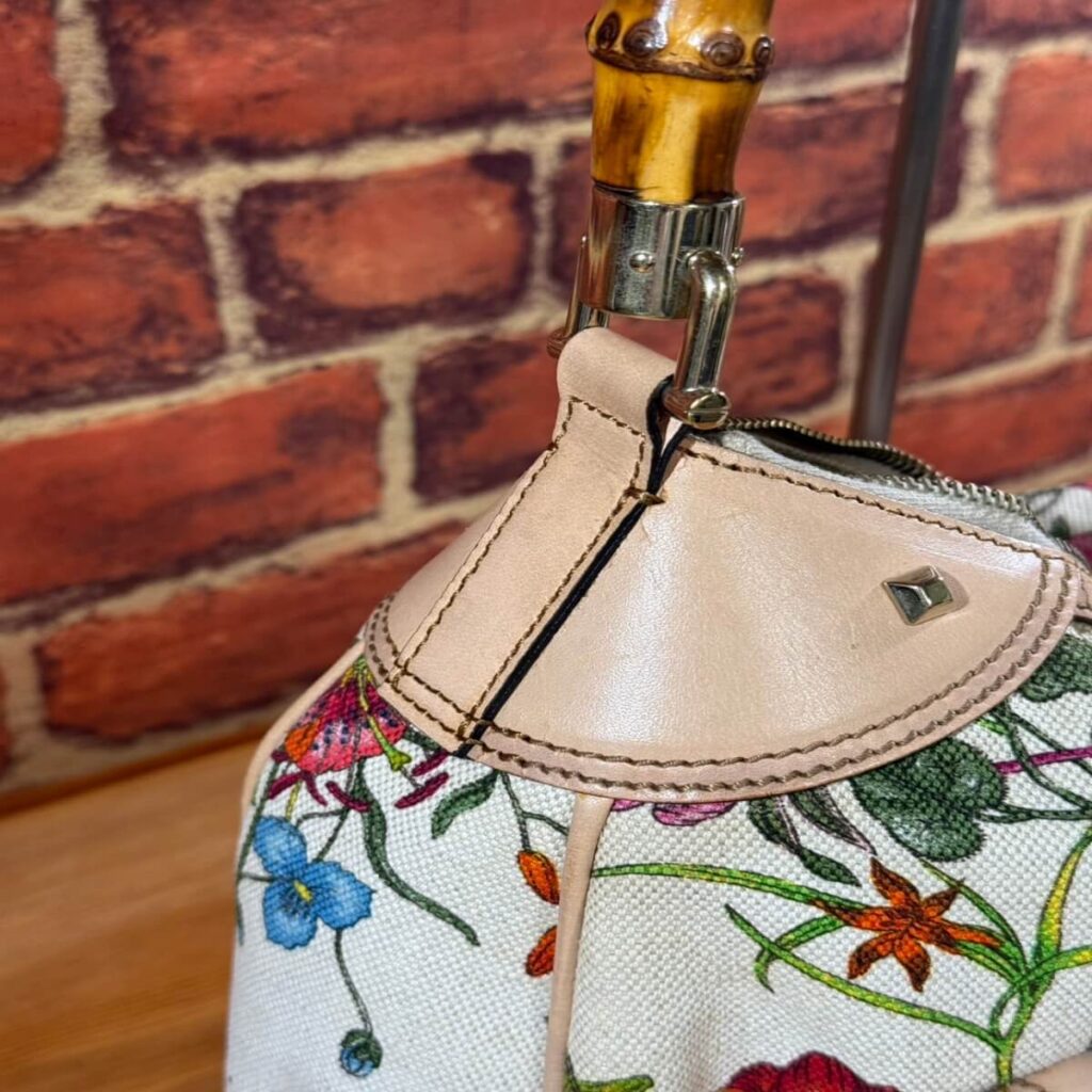 Floral fabric purse with beige leather trim and visible zipper, photographed against a brick wall.