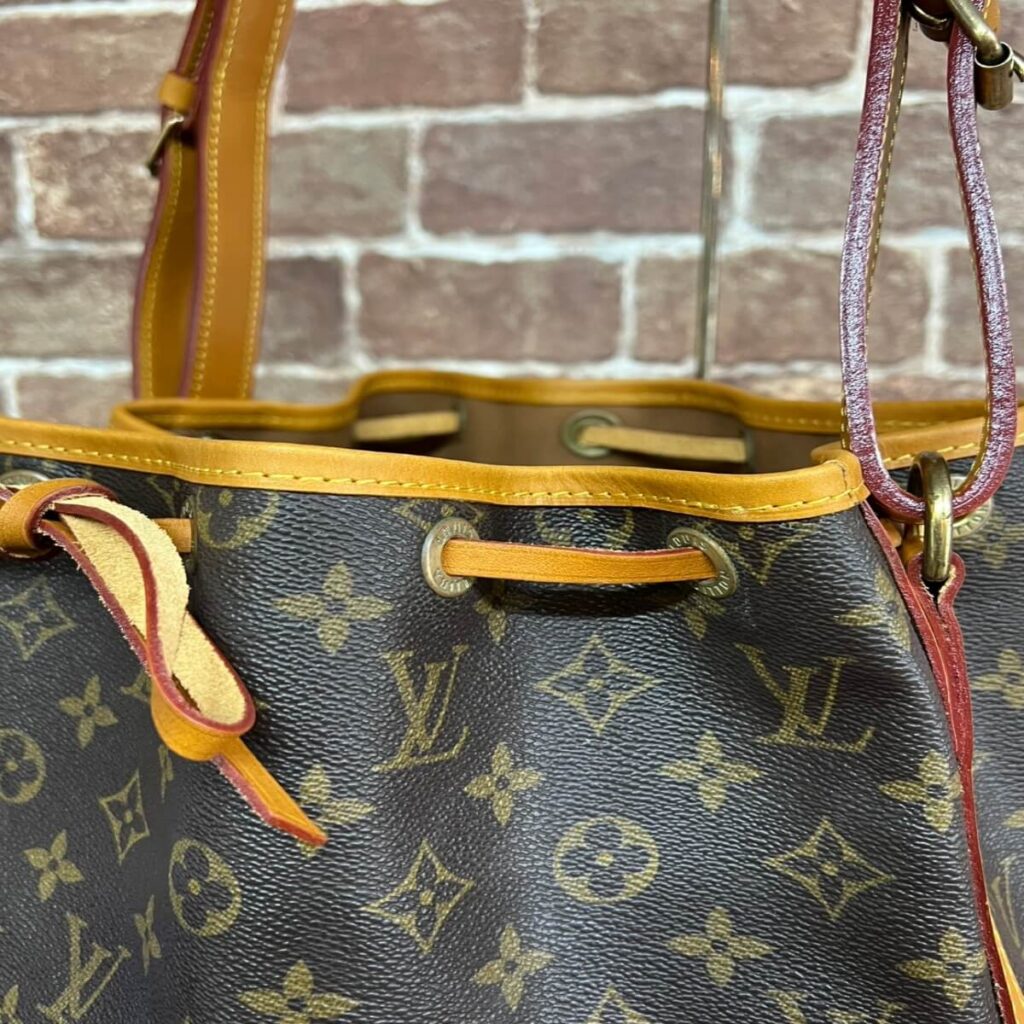 Louis Vuitton monogram canvas handbag with tan leather trim and drawstring closure on a brick background