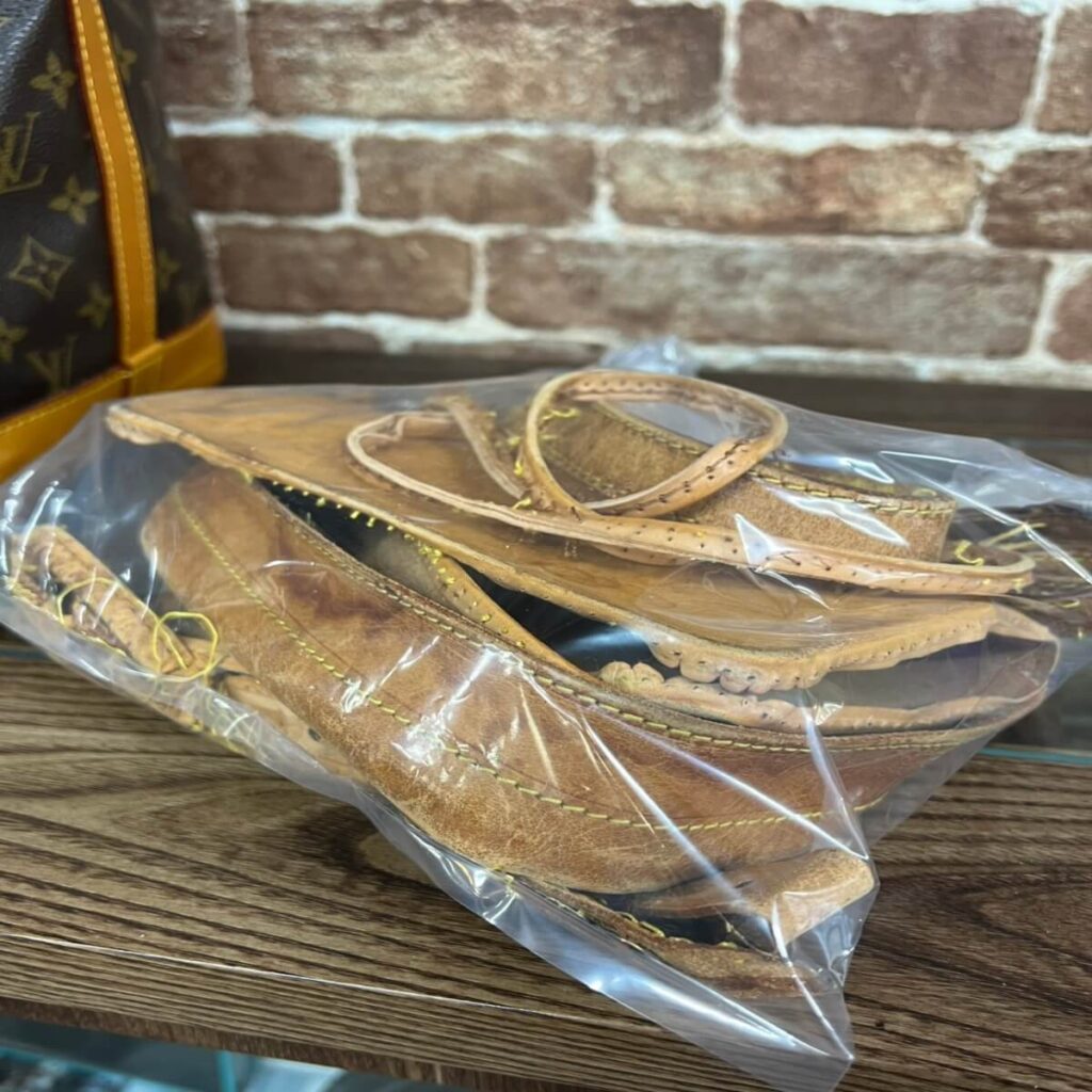 Brown leather sandals in a clear plastic bag on a wooden table, brick wall background.