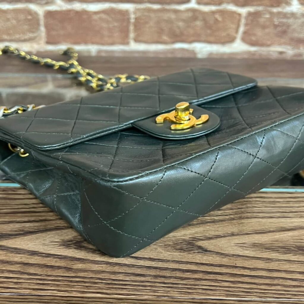 Black quilted leather handbag with a gold turn-lock clasp and chain strap on a wooden surface